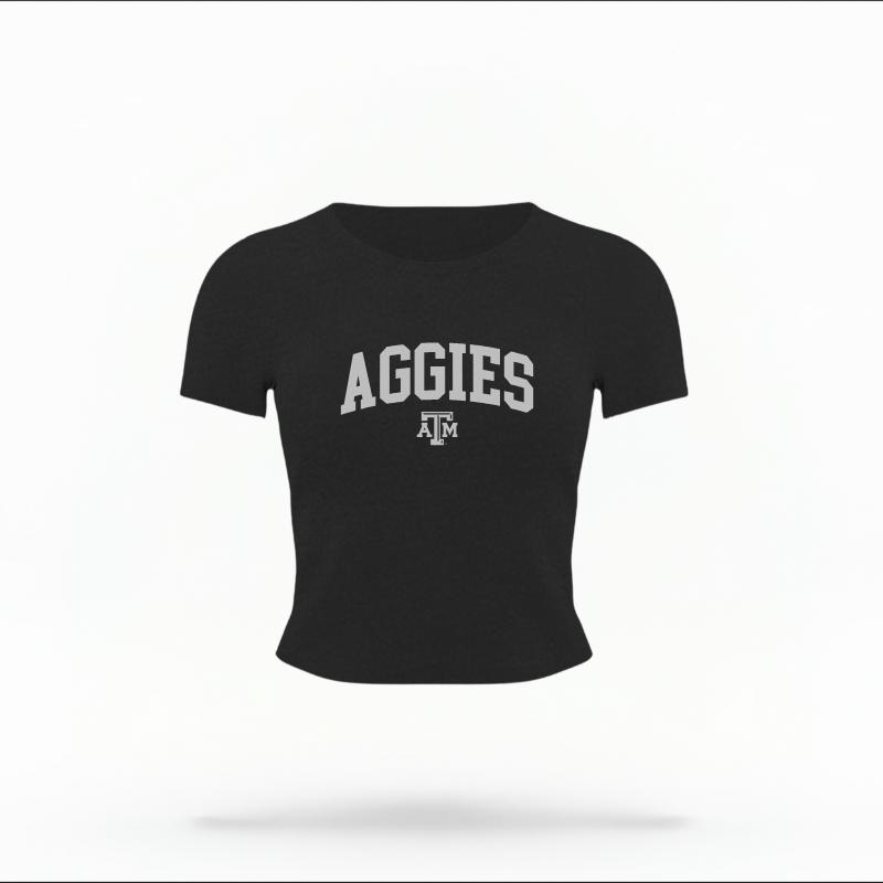 The Black Female Aggies Varsity Women's Baby Tee is set against a Ghost - White Studio background. The Aggies Varsity graphic is in a Varsity style.