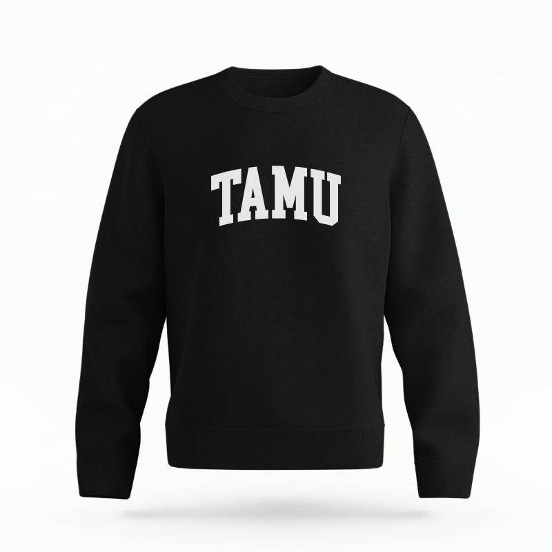 The Black Unisex TAMU Varsity Organic Cotton Crewneck is set against a Ghost - White Studio background. The TAMU Varsity graphic is in a Sports Graphics style.