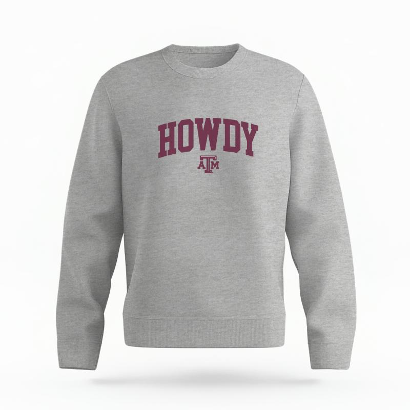 The Heather Grey Unisex Howdy Varsity Organic Cotton Crewneck is set against a Ghost - White Studio background. The Howdy Varsity graphic is in a Sports Graphics style.
