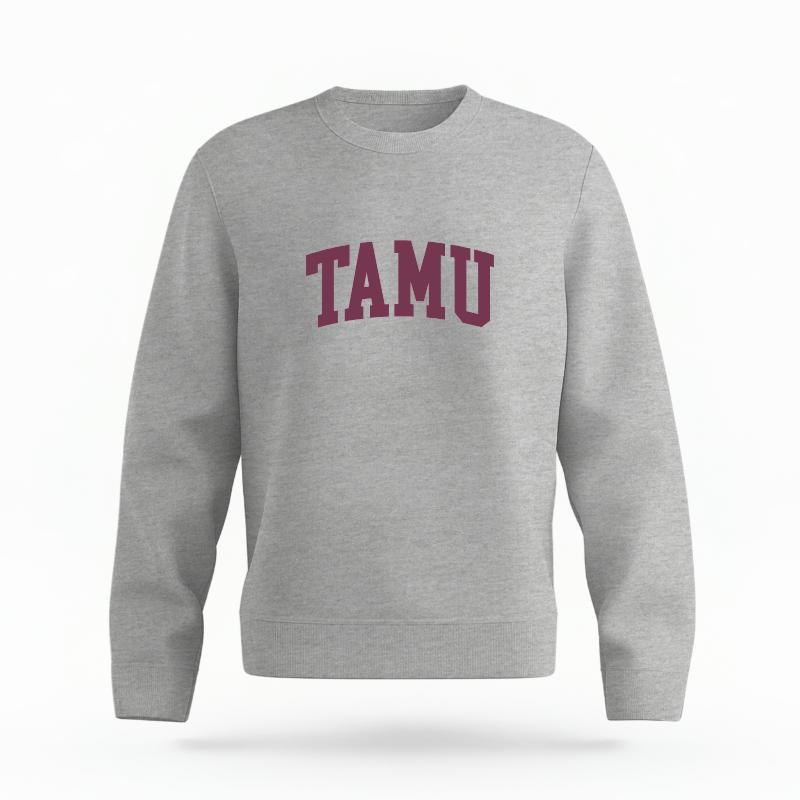 The Heather Grey Unisex TAMU Varsity Organic Cotton Crewneck is set against a Ghost - White Studio background. The TAMU Varsity graphic is in a Sports Graphics style.