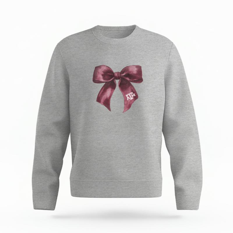The Heather Grey Unisex Texas A&M Coquette Bow Organic Cotton Crewneck is set against a Ghost - White Studio background. The Texas A&M Coquette Bow graphic is in a Coquette style.