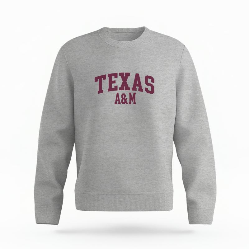 The Heather Grey Unisex Texas A&M Varsity Organic Cotton Crewneck is set against a Ghost - White Studio background. The Texas A&M Varsity graphic is in a Sports Graphics style.