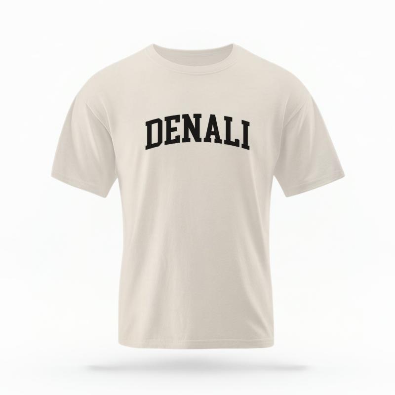The Ivory Unisex Denali Alaska Varsity T-shirt is set against a Ghost - White Studio background. The Denali Alaska Varsity graphic is in a Varsity style.