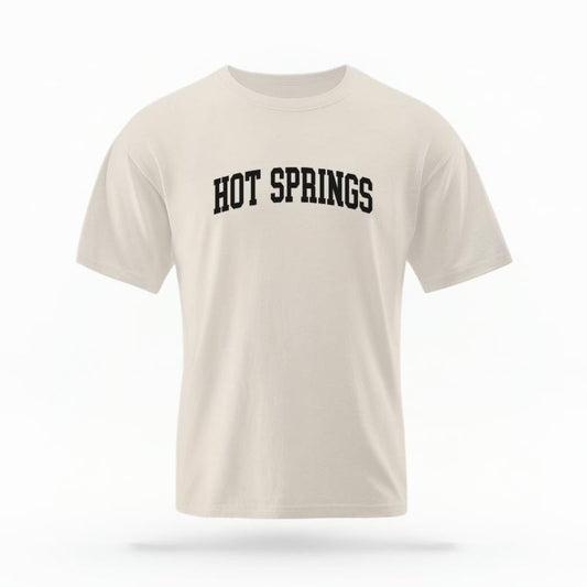 The Ivory Unisex Hot Springs AR Varsity T-shirt is set against a Ghost - White Studio background. The Hot Springs AR Varsity graphic is in a Varsity style.