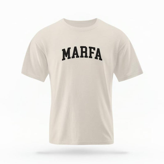 The Ivory Unisex Marfa Varsity T-shirt is set against a Ghost - White Studio background. The Marfa Varsity graphic is in a Varsity style.