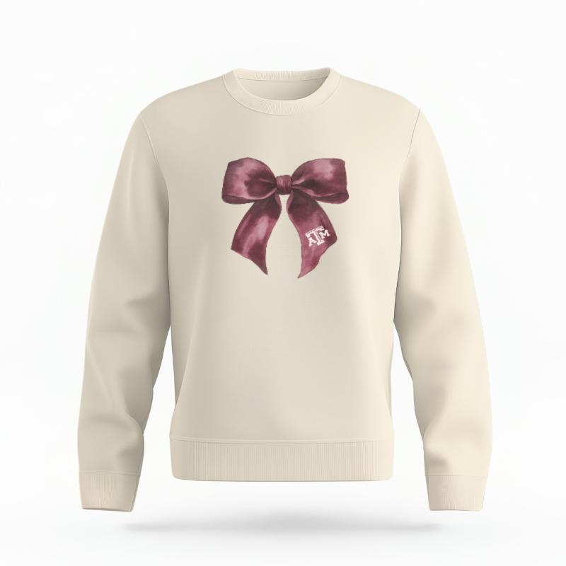The Ivory Unisex Texas A&M Coquette Bow Organic Cotton Crewneck is set against a Ghost - White Studio background. The Texas A&M Coquette Bow graphic is in a Coquette style.