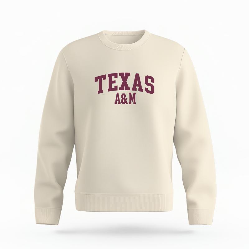 The Ivory Unisex Texas A&M Varsity Organic Cotton Crewneck is set against a Ghost - White Studio background. The Texas A&M Varsity graphic is in a Sports Graphics style.
