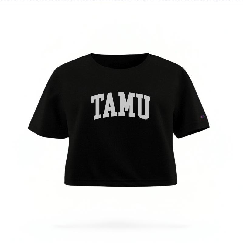 The Black Female TAMU Varsity Women's Boxy Crop Top is set against a Ghost - White Studio background.  The TAMU Varsity graphic is in a Sports Graphics style. 