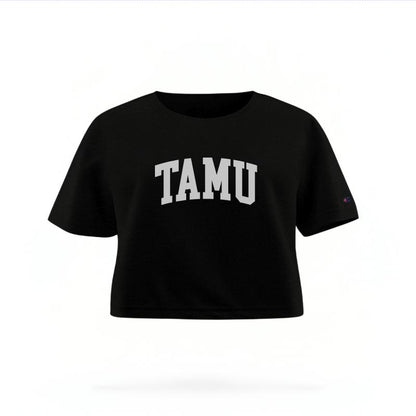 The Black Female TAMU Varsity Women's Boxy Crop Top is set against a Ghost - White Studio background.  The TAMU Varsity graphic is in a Sports Graphics style. 