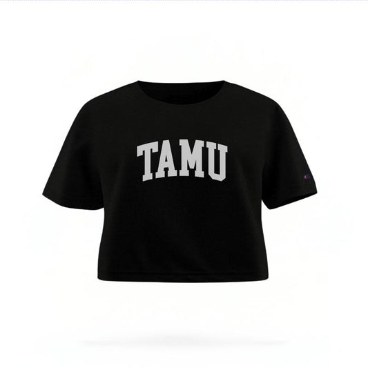 The Black Female TAMU Varsity Women's Boxy Crop Top is set against a Ghost - White Studio background.  The TAMU Varsity graphic is in a Sports Graphics style. 