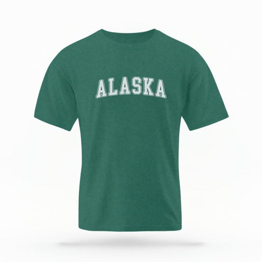 The Blue Spruce Unisex Alaska Varsity T-shirt is set against a Ghost - White Studio background.  The Alaska Varsity graphic is in a Varsity style. 