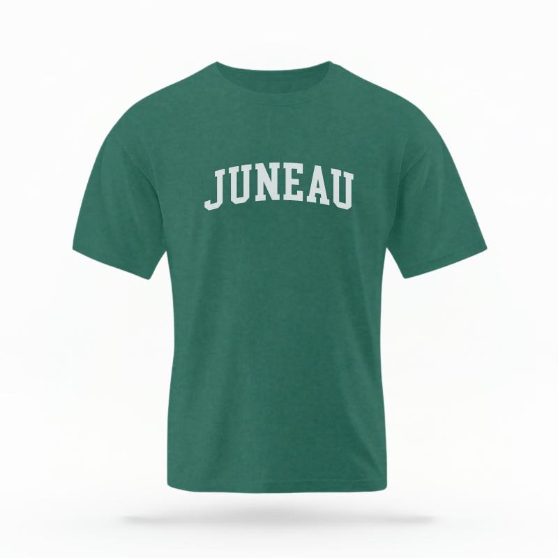 The Blue Spruce Unisex Juneau Alaska Varsity T-shirt is set against a Ghost - White Studio background.  The Juneau Alaska Varsity graphic is in a Varsity style. 