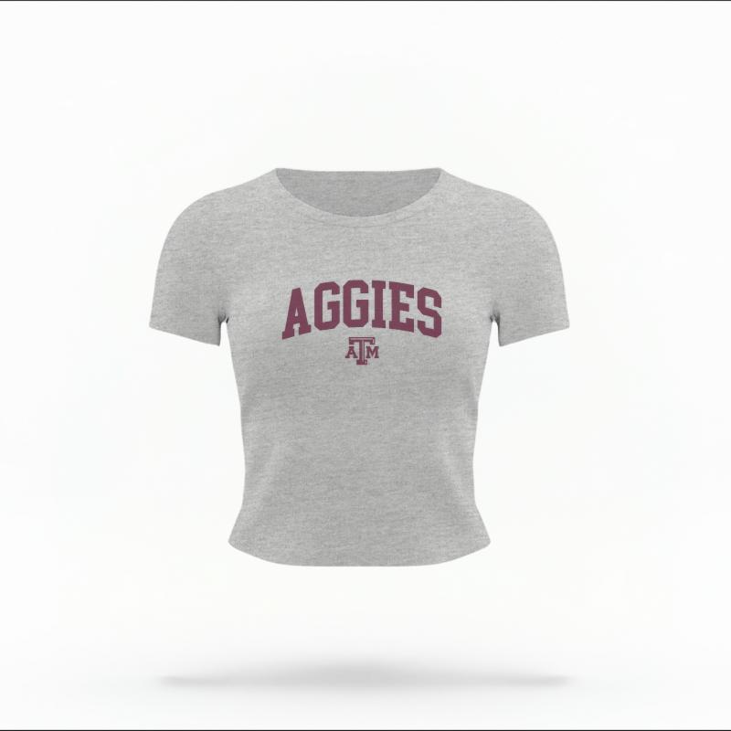 The Heather Grey Female Aggies Varsity Women's Baby Tee is set against a Ghost - White Studio background.  The Aggies Varsity graphic is in a Varsity style. 