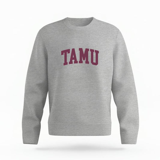 The Heather Grey Unisex TAMU Varsity Organic Cotton Crewneck is set against a Ghost - White Studio background.  The TAMU Varsity graphic is in a Sports Graphics style. 