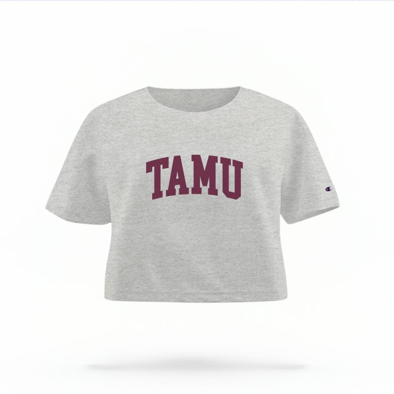 The Heather Grey Female TAMU Varsity Women's Boxy Crop Top is set against a Ghost - White Studio background.  The TAMU Varsity graphic is in a Sports Graphics style. 