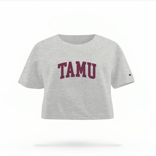 The Heather Grey Female TAMU Varsity Women's Boxy Crop Top is set against a Ghost - White Studio background.  The TAMU Varsity graphic is in a Sports Graphics style. 