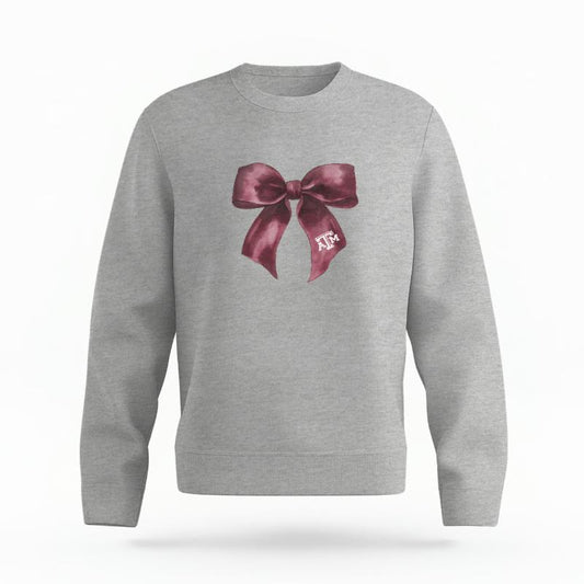 The Heather Grey Unisex Texas A&M Coquette Bow Organic Cotton Crewneck is set against a Ghost - White Studio background.  The Texas A&M Coquette Bow graphic is in a Coquette style. 
