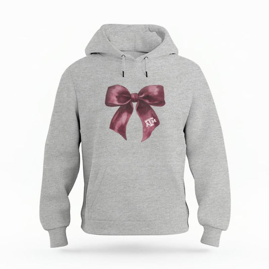The Heather Grey Unisex Texas A&M Coquette Bow Organic Cotton Hoodie is set against a Ghost - White Studio background.  The Texas A&M Coquette Bow graphic is in a Coquette style. 