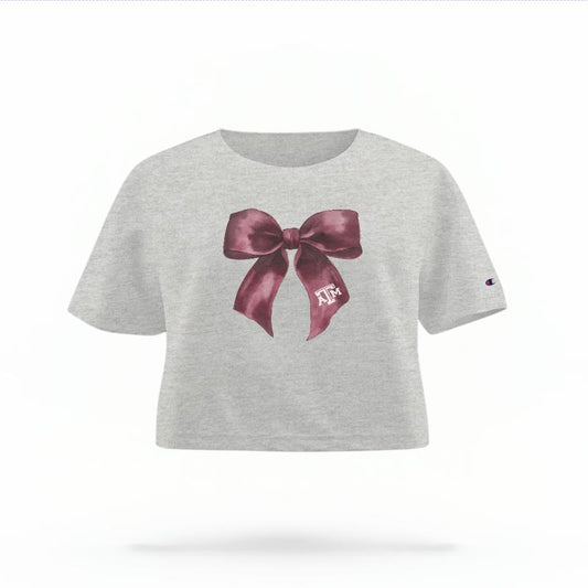 The Heather Grey Female Texas A&M Coquette Bow Women's Boxy Crop Top is set against a Ghost - White Studio background.  The Texas A&M Coquette Bow graphic is in a Coquette style. 