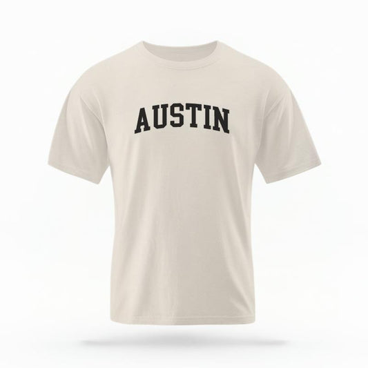The Ivory Unisex Austin Varsity T-shirt is set against a Ghost - White Studio background.  The Austin Varsity graphic is in a Varsity style. 