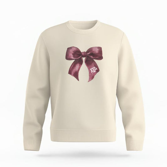 The Ivory Unisex Texas A&M Coquette Bow Organic Cotton Crewneck is set against a Ghost - White Studio background.  The Texas A&M Coquette Bow graphic is in a Coquette style. 