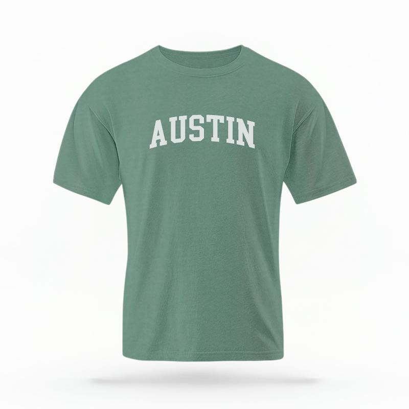 The Light Green Unisex Austin Varsity T-shirt is set against a Ghost - White Studio background.  The Austin Varsity graphic is in a Varsity style. 