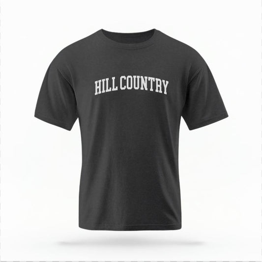 The Pepper Unisex Hill Country Varsity T-shirt is set against a Ghost - White Studio background.  The Hill Country Varsity graphic is in a Varsity style. 