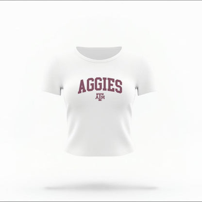 The White Female Aggies Varsity Women's Baby Tee is set against a Ghost - White Studio background.  The Aggies Varsity graphic is in a Varsity style. 