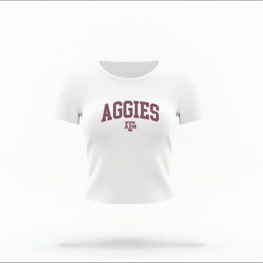 The White Female Aggies Varsity Women's Baby Tee is set against a Ghost - White Studio background.  The Aggies Varsity graphic is in a Varsity style. 