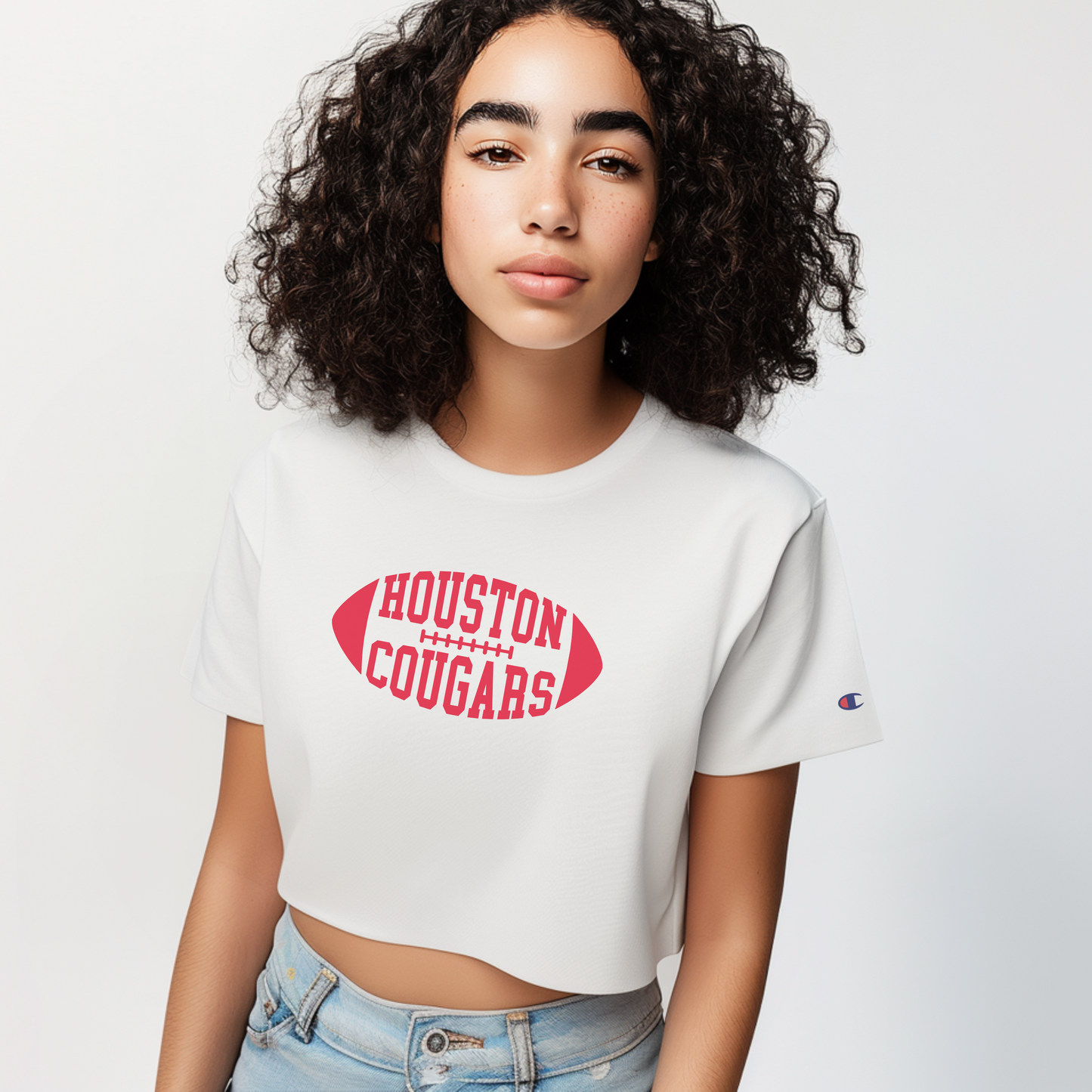 The White Female Houston Cougars Football Women's Boxy Crop Top is worn by a model.  The Houston Cougars Football graphic is in a Varsity style. 