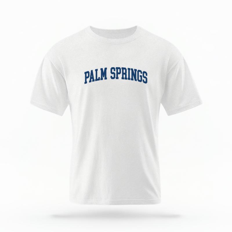 The White Unisex Palm Springs CA Varsity T-shirt is set against a Ghost - White Studio background.  The Palm Springs CA Varsity graphic is in a Varsity style. 