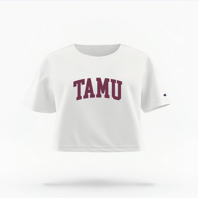 The White Female TAMU Varsity Women's Boxy Crop Top is set against a Ghost - White Studio background.  The TAMU Varsity graphic is in a Sports Graphics style. 