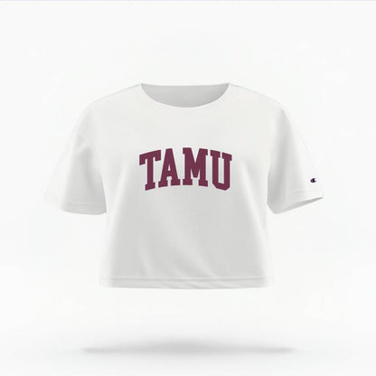 The White Female TAMU Varsity Women's Boxy Crop Top is set against a Ghost - White Studio background.  The TAMU Varsity graphic is in a Sports Graphics style. 