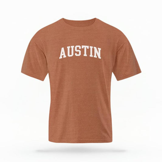 The Yam Unisex Austin Varsity T-shirt is set against a Ghost - White Studio background.  The Austin Varsity graphic is in a Varsity style. 
